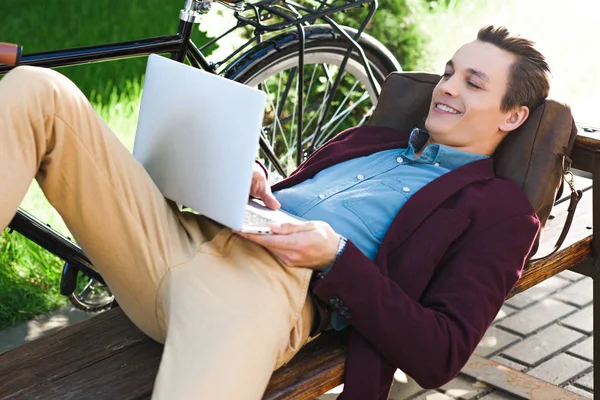 Sorrindo Jovem Usando Laptop Enquanto Deitado Banco — Fotografia de Stock