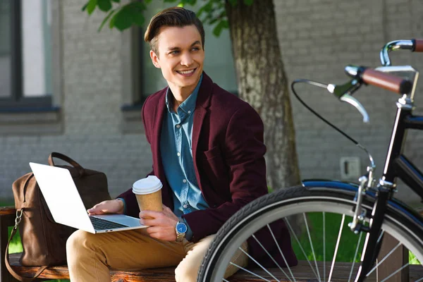 Knappe Lachende Jongeman Met Koffie Gaan Met Behulp Van Laptop — Gratis stockfoto