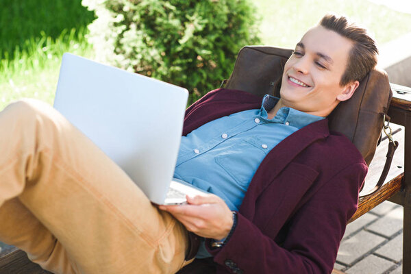 happy young freelancer lying on bench and using laptop