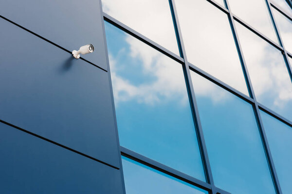 Glass facade of modern office building with security camera and reflected clouds