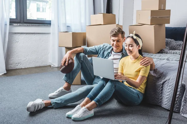 幸せな若いカップルの寝室の床に座って 新しい家に移動しながらノート パソコンを使用して — ストック写真