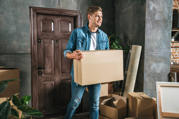 handsome young man carrying box while moving into new house