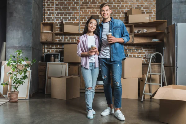 快乐的年轻夫妇与纸杯咖啡站在厨房 而搬进新家 — 图库照片