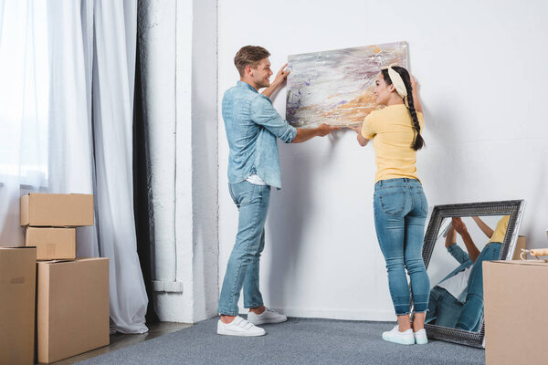 beautiful young couple hanging picture on wall together while moving into new home
