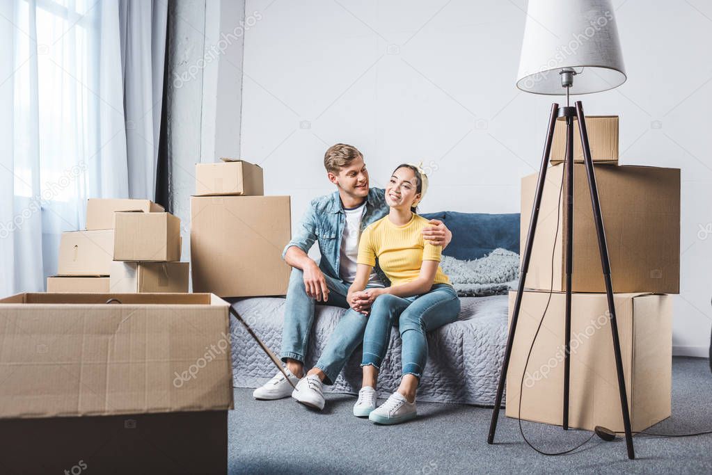 beautiful young couple sitting on bed after moving into new home surrounded with boxes
