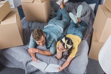 high angle view of happy young couple with photo album lying on bed while moving into new home clipart