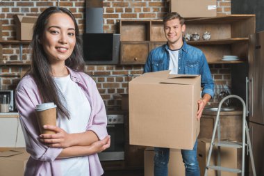 beautiful young couple with boxes and coffee to go moving into new home clipart