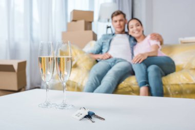 beautiful young couple relaxing on couch while moving into new home with champagne glasses and keys on foreground clipart