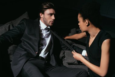 Genç çok ırklı seksi çift kanepe koyu arka plan üzerinde siyah giyim