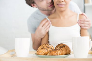 seçici odak ahşap tepsi ve çok ırklı çift evde kahvaltı