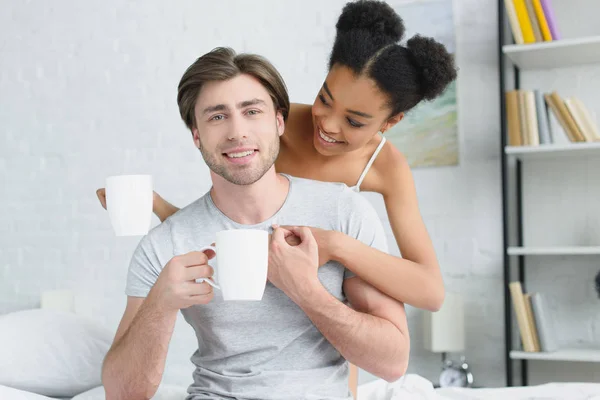 Portrait Smiling Multiracial Couple Cups Coffee Bed Morning — Free Stock Photo