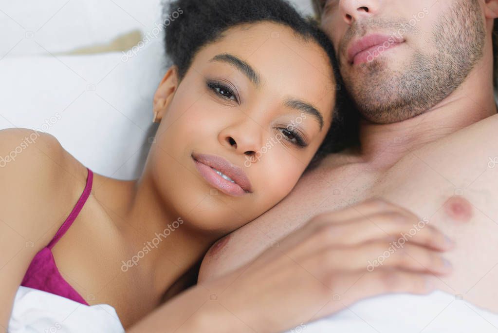 partial view of multiethnic young couple in love lying in bed together in morning