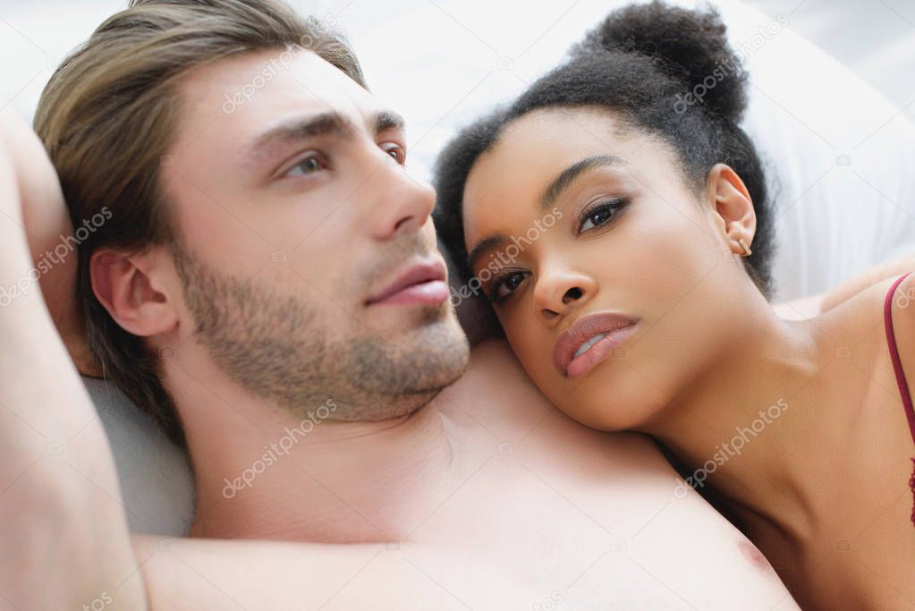 portrait of multiethnic young couple in love lying in bed together in morning