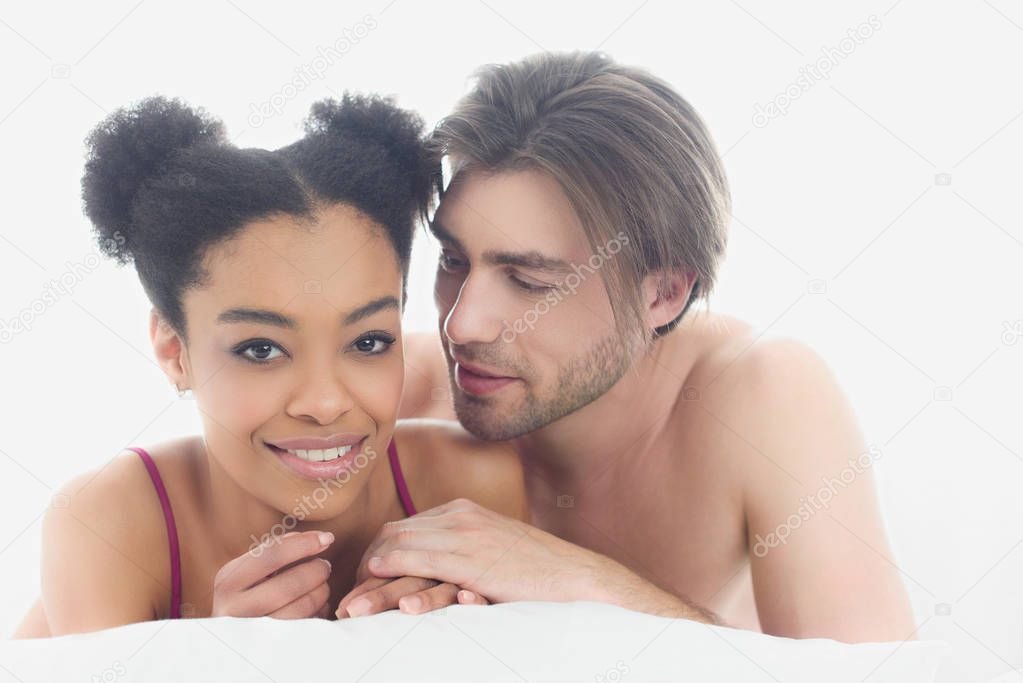 portrait of young interracial couple resting in bed together in morning at home