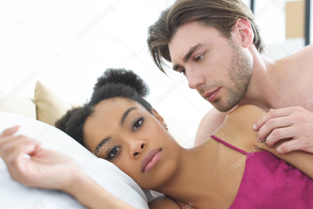 portrait of young interracial couple lying in bed in morning at home