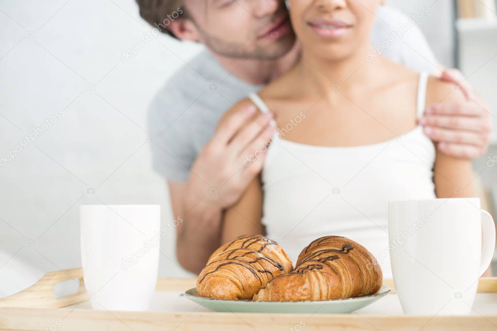 selective focus of breakfast on wooden tray and multiethnic couple at home