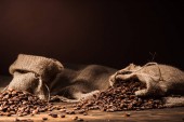sacks of coffee beans on rustic wooden table on dark brown background