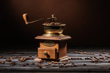 Vintage kahve değirmeni rustik ahşap masa üzerinde kahve çekirdekleri ile dökülen