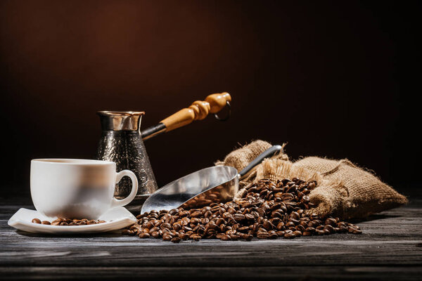 Кофейная чашка с совок и cezve на куче кофейных зерен и на деревенском деревянном столе
