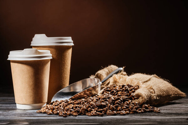 close-up shot of paper cups with scoop and heap of coffee beans on rustic wooden table