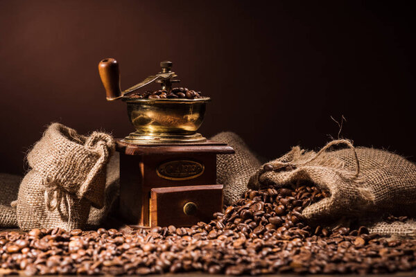 vintage coffee grinder with sacks of coffee on dark brown background