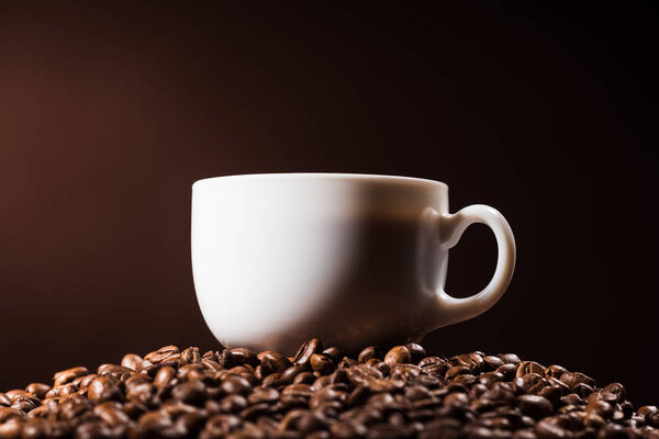 close-up shot of cup standing on heap of coffee beans on dark brown background