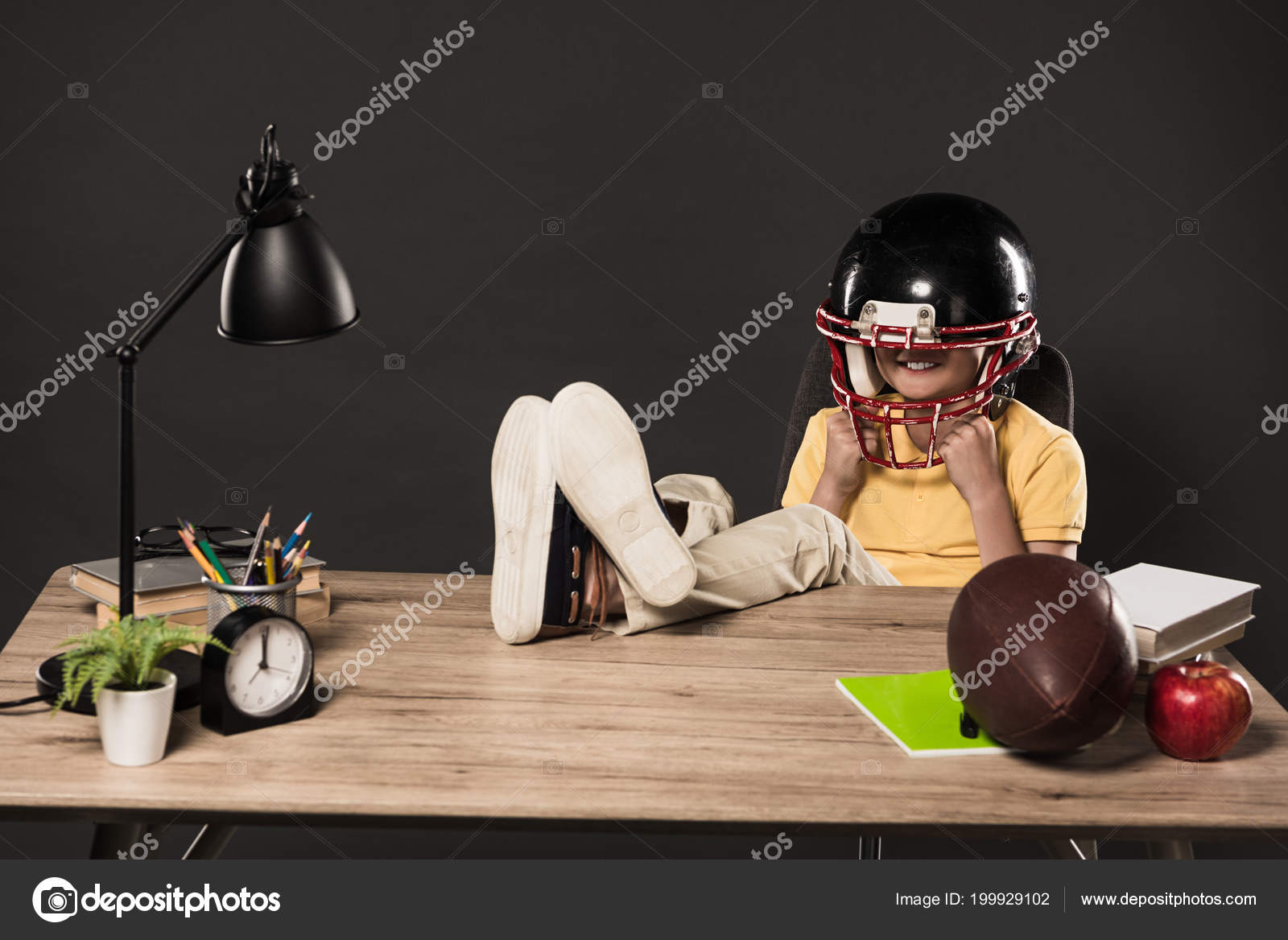 Smiling American Football Helmet Sitting Legs Table Ball Smiling In American Football Helmet Sitting With Legs On Table Ball Books Plant Lamp Colour Pencils Apple Clock And Textbook Grey