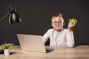 mutlu çocuğu armut tutarak ve bitki ve gri arka plan üzerinde lamba ile masada dizüstü kullanarak gözlük 