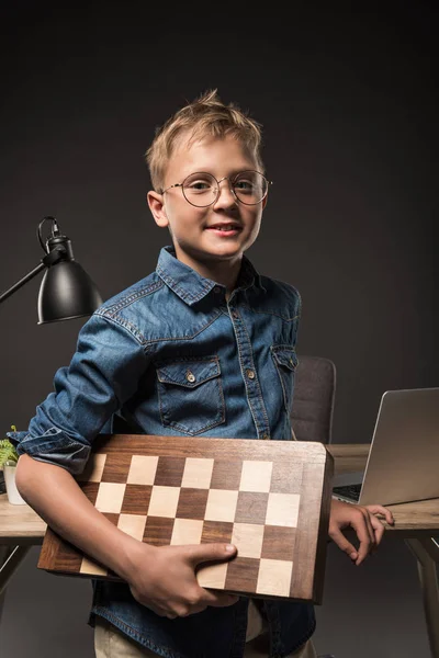 Smiling Little Boy Eyeglasses Holding Chessboard Table Laptop Lamp Grey — Free Stock Photo