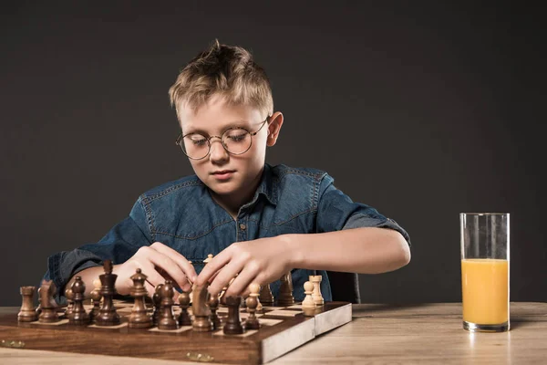 Ориентированный Маленький Мальчик Играет Шахматы Столом Стаканом Сока Сером Фоне — стоковое фото