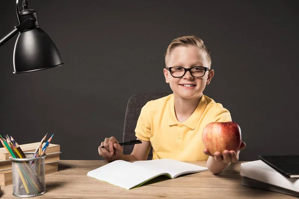 Colegial Anteojos Sosteniendo Manzana Haciendo Deberes Mesa Con Libros Lámpara — Foto de stock gratuita