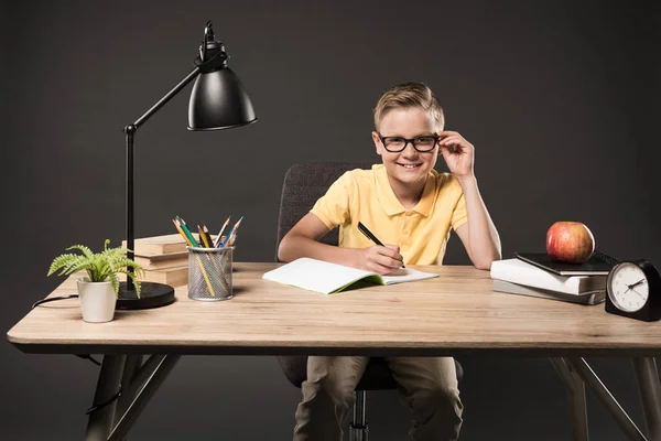 ランプ 色鉛筆 アップル 灰色の背景の教科書とのテーブルで宿題をしている眼鏡の小さな男子生徒 — ストック写真