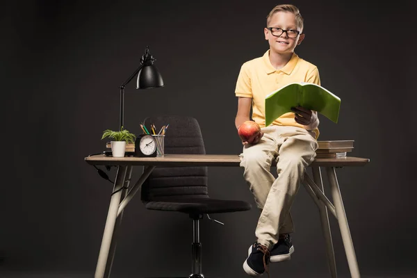 Menino Escola Óculos Segurando Maçã Fazendo Lição Casa Enquanto Sentado — Fotografia de Stock