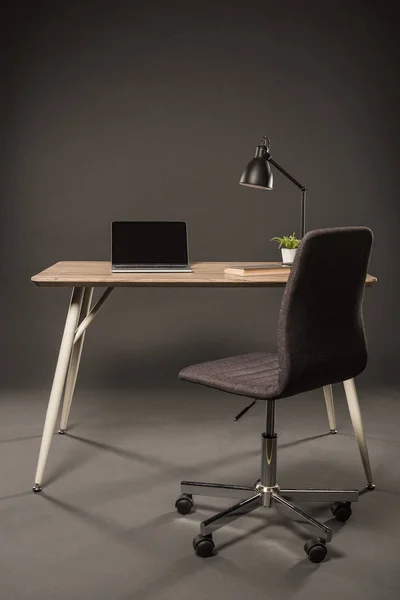 chair and table with lamp, plant, book and laptop with blank screen on grey background