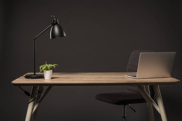 close up view of chair and table with lamp, plant, book and laptop on grey background 