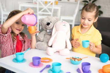 adorable little sisters pretending to have tea party together at home clipart