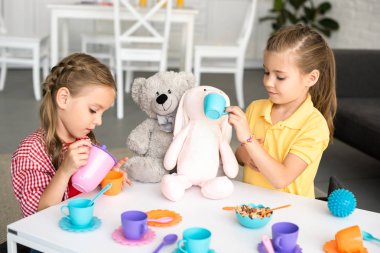 adorable little sisters pretending to have tea party together at home clipart