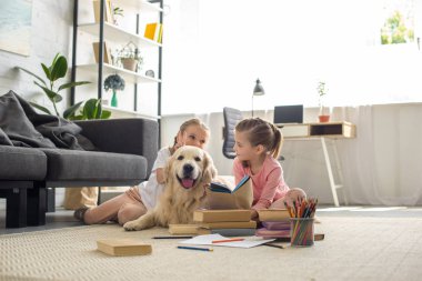 cute little sisters with books and golden retriever dog near by sitting on floor at home clipart