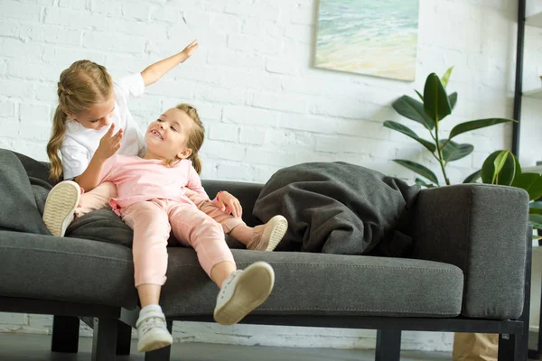 自宅のソファの上楽しんで愛らしい小さな子供たち — ストック写真