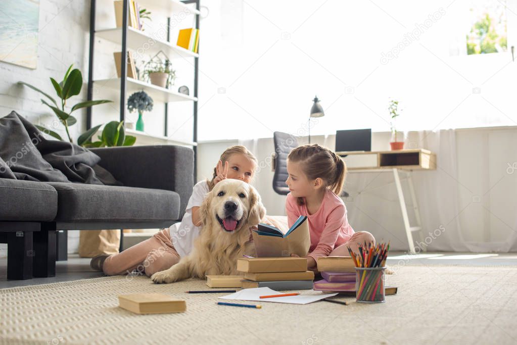 cute little sisters with books and golden retriever dog near by sitting on floor at home