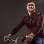 Low angle view of smiling man in eyeglasses riding bike and looking away isolated on black