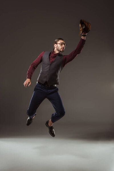 young businessman in baseball glove jumping and catching ball on black