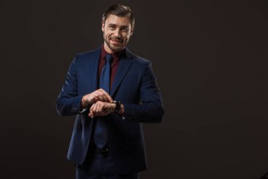 Kol saati kontrol ve siyahta izole kamera gülümseyen yakışıklı işadamı