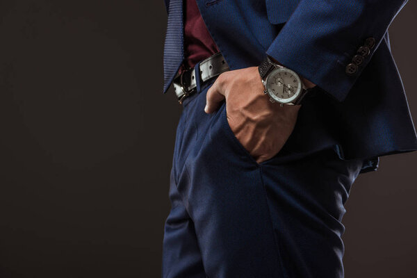 обрезанный снимок бизнесмена с наручными часами, стоящими с рукой в кармане изолированы на черном

