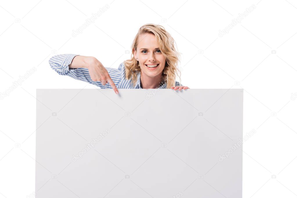 smiling attractive woman pointing on blank placard isolated on white