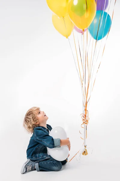 adorable boy looking at bundle of balloons on white