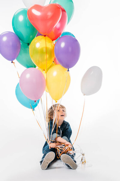 happy adorable boy holding bundle of balloons with helium on white