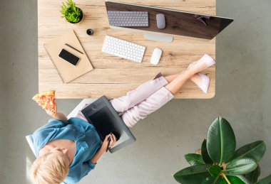 pizza yemek ve evde masada bacakları ile grafik tablet kullanarak şık kadın Freelancer üstten görünüm