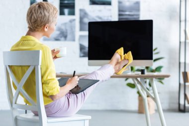 kahve içme ve masada ev ofis bilgisayarı ile grafik tablet kullanarak kadın Freelancer seçici odak 