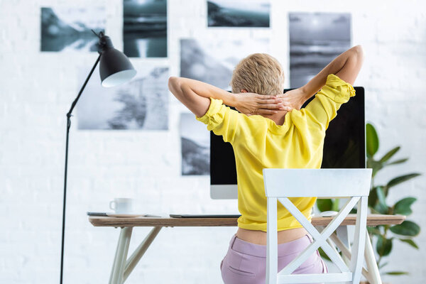 rear view of businesswoman doing stretch while sitting at table with computer at home 